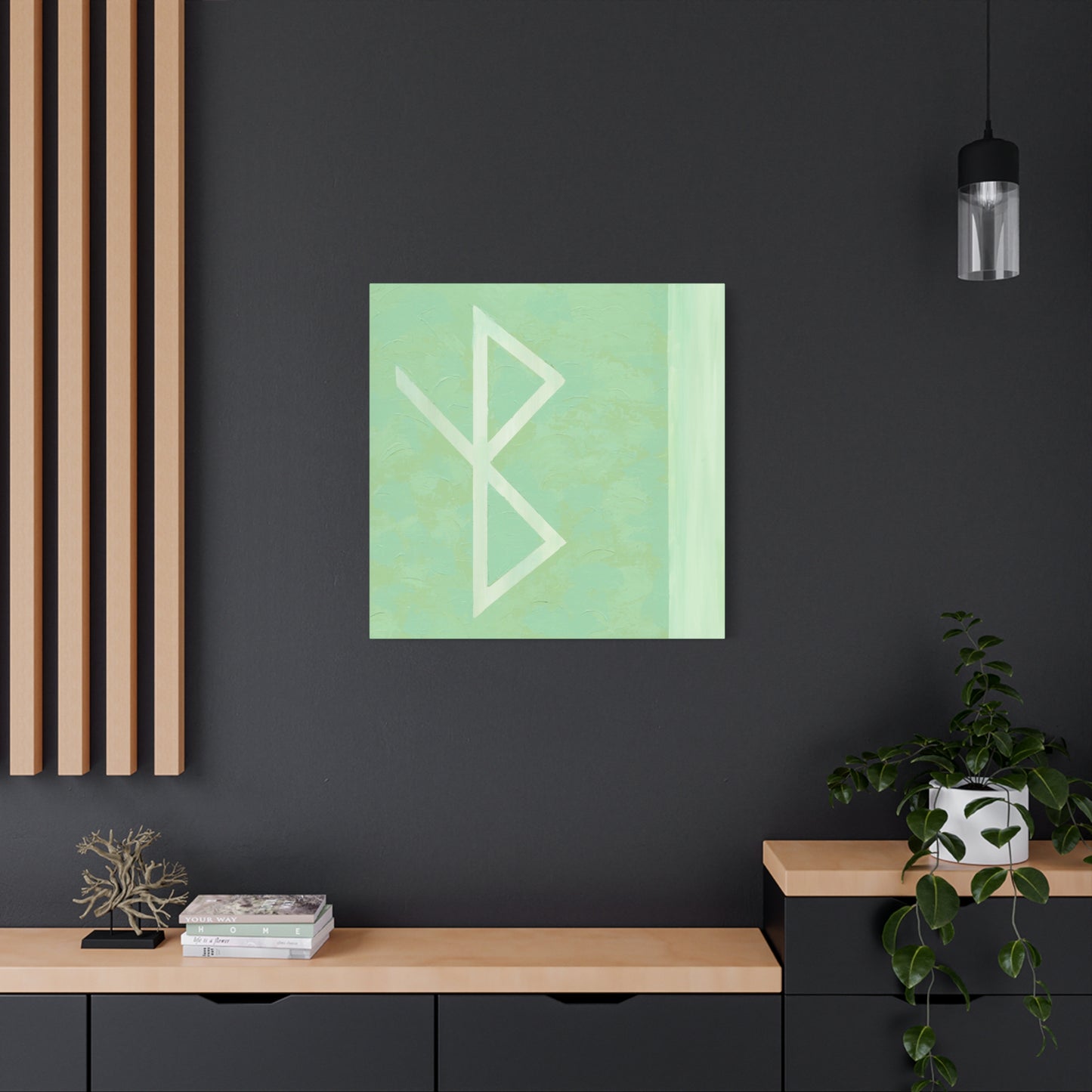 A square wall art print featuring a white bind rune symbol on a light mint green background, displayed on a dark charcoal wall above a wooden console table in a modern room setting.