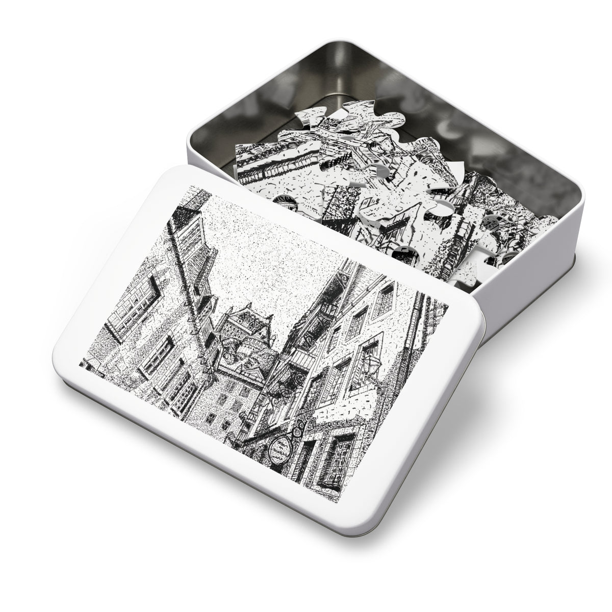 An open rectangular metal jigsaw puzzle box showing white puzzle pieces inside, with the lid displaying a black-and-white architectural illustration on a clean white background.