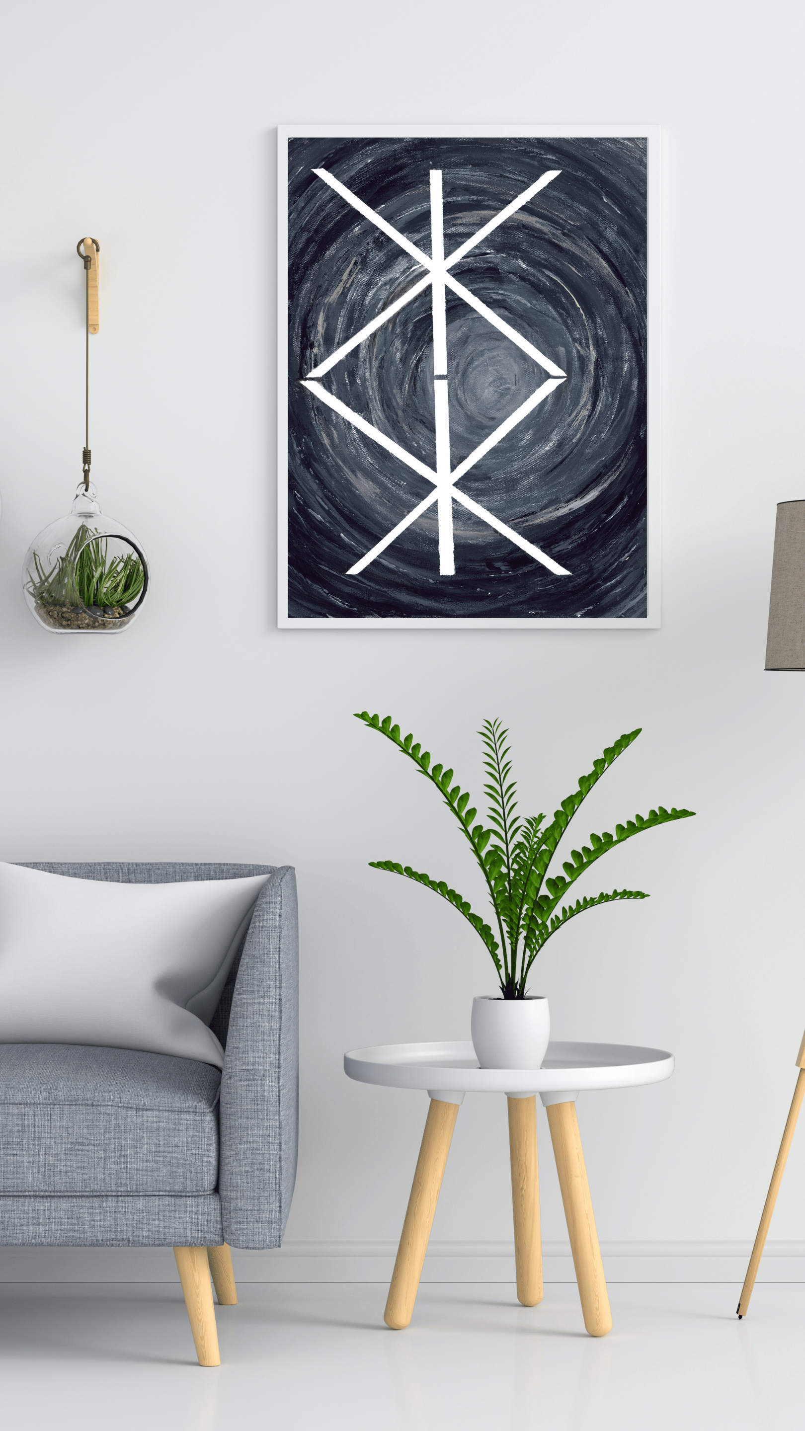 A framed abstract art print featuring a white geometric bind rune symbol over a dark swirling background, displayed on a white wall in a modern living room setting with a gray armchair, side table, and potted plant.