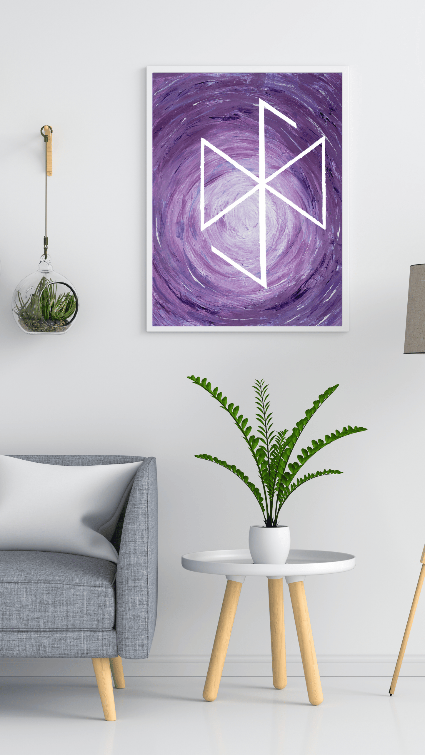 A framed wall art print featuring a white geometric rune symbol over a purple and lavender swirling background, displayed in a modern living room setting above a gray armchair and a small side table with a green plant.