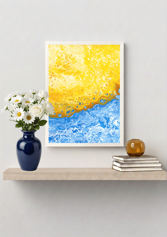 A white framed abstract art print featuring a yellow and blue textured design, displayed on a light wood floating shelf with a blue vase of white flowers and a small amber decorative vase on top of a stack of books against a light gray wall.